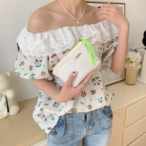 White lace lipstick pouch with neon green rope held by a hand in a bright room