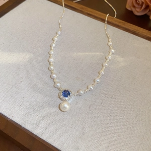 Dettaglio di collana di perle vintage con ciondolo in gemma blu su vassoio di lino