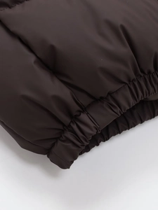 Detail of dark brown puffer vest featuring elastic hem and matte waterproof fabric