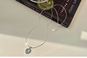 Macro view of light blue oval gemstone pendant on delicate silver snake chain