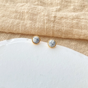 Macro shot of small round marble studs with golden plating on beige textile and white tray