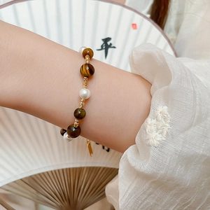 Detail of gold-plated tiger eye and pearl beaded bracelet worn on a female wrist