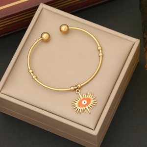 Detailed close-up of a gold-plated open bangle featuring an orange evil eye charm on a jewelry box