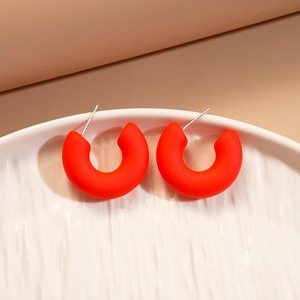 Detailed view of matte red C-shaped acrylic earrings with silver needles on textured tray