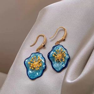 Gros plan détaillé de boucles d'oreilles fleur en émail bleu sur tissu en soie