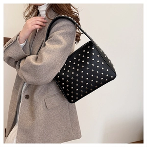 Detail view of the silver rivets on a black leather shoulder bag worn with a gray blazer