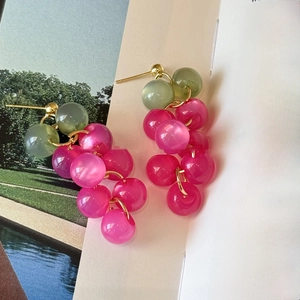 Détail de boucles d'oreilles grappes en résine rose et métal doré sur livre