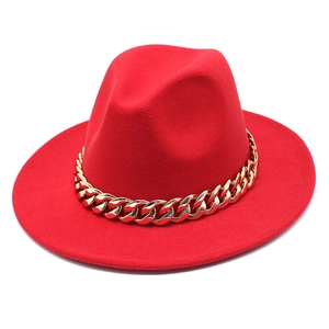 Detailed close-up of a red fedora hat featuring a chunky gold chain accessory on felt