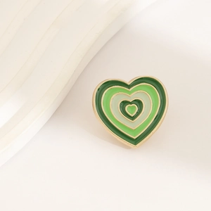 Detail of green gradient enamel heart brooch with polished metallic frame on beige background