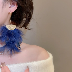 Macro detail of long dark blue feather earrings with a textured golden semi-circle stud