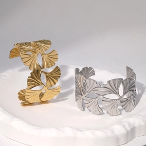 Detailed close-up of gold and silver ginkgo leaf open bracelets on a white tray