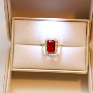 Macro shot of rectangular red gemstone halo ring with gold band and gift box