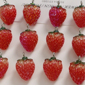 Macro shot of red resin strawberry charms with green leaves and metal rings for DIY jewelry