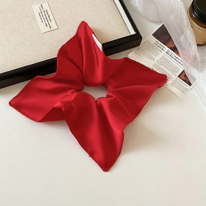Elegant red silk scrunchie with soft folds displayed on a minimalist aesthetic desk setup