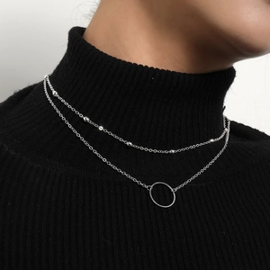 Close-up of a double-layered silver chain necklace with a round ring pendant and bead details