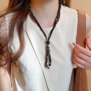 Close-up of black fabric scarf necklace with white patterns and a deep red bead detail