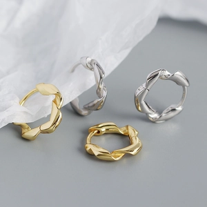 Macro shot of gold and silver irregular twisted hoop earrings on white textured background