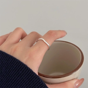 Close-up of minimalist silver wave ring with polished finish on model holding ceramic cup
