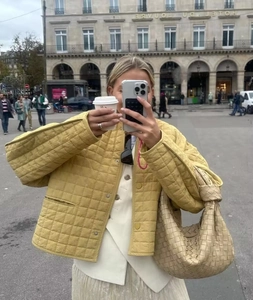 Détail d'une veste matelassée jaune moutarde avec un sac hobo tissé beige élégant
