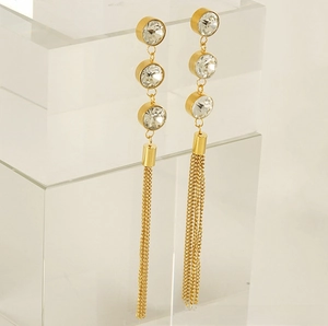 Détail des boucles d'oreilles à pompons dorés avec trois zircons scintillants