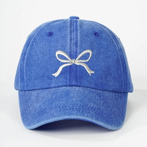 Close-up of bow embroidery detail on washed denim blue baseball cap with high texture