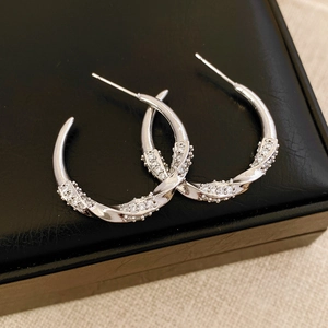 Dettaglio orecchini a C ritorti placcati oro 18K con zirconi su un portagioie elegante