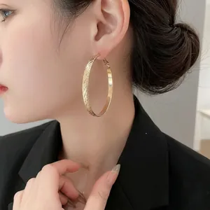 Large gold hoop earrings with brushed metal finish on model in a black blazer suit