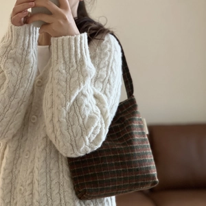 Detail of red and green plaid wool shoulder bag styled with white knit cardigan