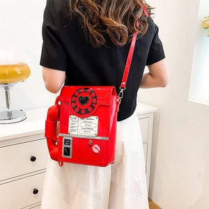 Bright red retro telephone crossbody bag in shiny patent leather on model for size scale