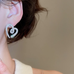 Close-up of silver snake-shaped heart earrings with clear zircon and green gemstone eyes