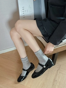 Close-up of black patent leather Mary Jane shoes with silver bead buckle and knit socks