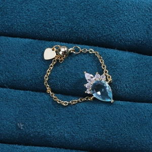 Macro detail of a gold teardrop ring with blue gemstone and micro-pave zircons