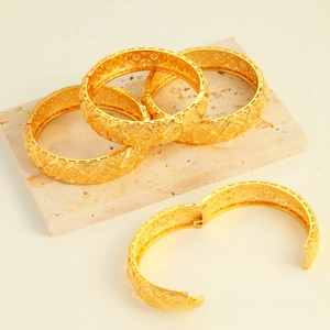 Detail of hollowed floral pattern gold bracelets with hinge clasp on stone surface