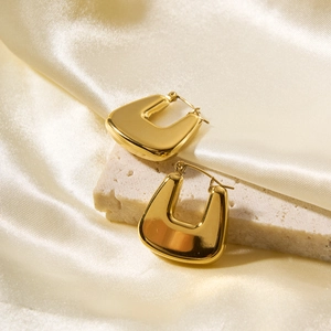 Detail of golden U-shaped stainless steel earrings on stone and silk background