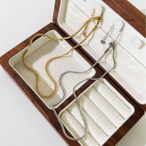 Minimalist titanium steel snowflake link necklaces in gold and silver on a wooden box