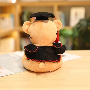 Rear view of graduation teddy bear plush wearing a black academic gown and cap on wood