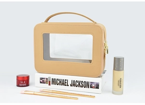 Detail view of beige portable makeup bag with clear PVC window and gold zipper accents