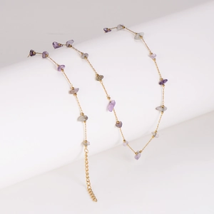 Gold chain necklace with purple and gray stones draped on a white pedestal