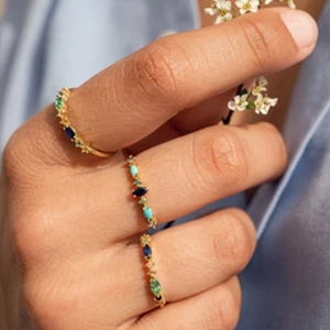 Close-up of three gold rings with emerald and sapphire marquise cut stones worn by model