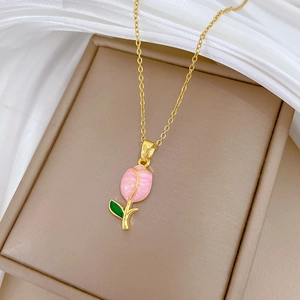Detailed shot of a gold necklace featuring a pink tulip pendant with green leaves