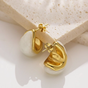 Detailed macro view of gold-plated drop earrings with white stone on a textured stone