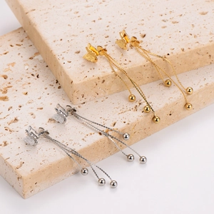 Détail de boucles d'oreilles papillon dorées et argentées avec franges sur travertin