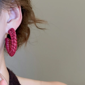 Close-up of burgundy woven leather texture C-shaped hoop earrings worn on ear
