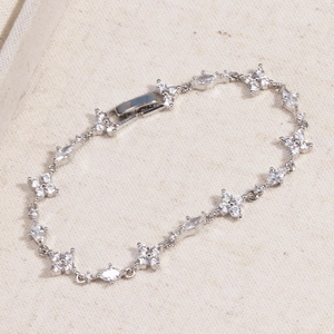 Macro detail of silver clover bracelet with marquise zircon stones on textile background