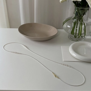 Detail of elegant long pearl necklace with golden clasp laid on a white minimalist table