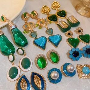 Collection of vintage gold earrings with green gemstones and pearls on silk background
