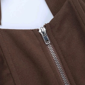 Detail van de zilveren metalen rits op de bruine haltertop met rugloos ontwerp en textuur