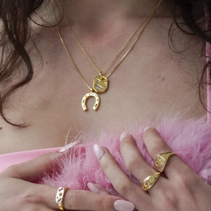 Close-up of layered gold U-shape horseshoe necklace and colorful stone rings on a model