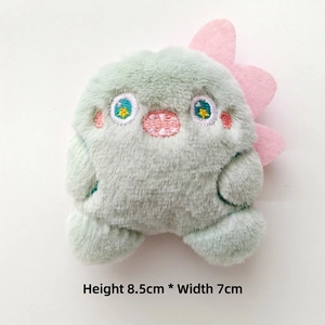 Detail view of a 8.5cm tall mint green plush monster charm with pink fins and embroidery