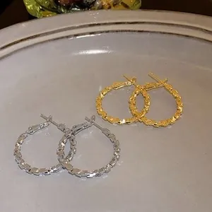 Detail view of large gold and silver hoop earrings with a textured hammered metal finish